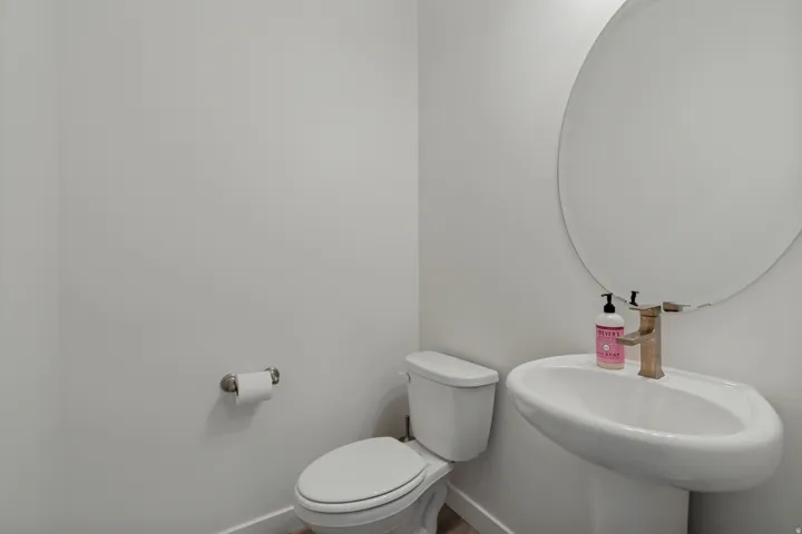 Pedestal sink with a single-handle faucet, round mirror, and white toilet