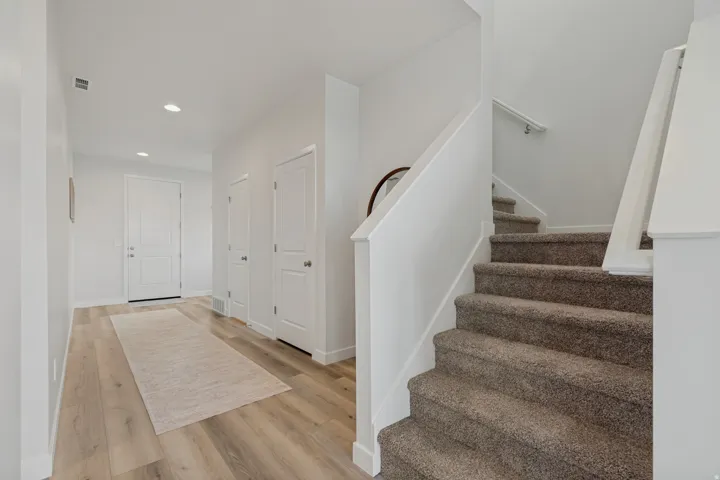 Light-toned wood-finish flooring, recessed lighting, white panel doors, and a carpeted staircase