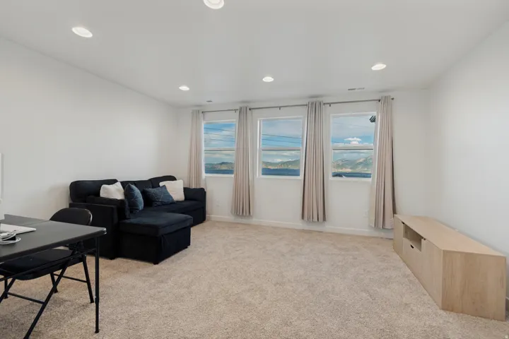 Recessed lighting, light-toned carpeting, three windows, and a wood-finish media console