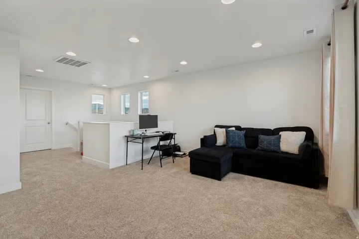 Carpeted loft space with recessed lighting, multiple windows, and a white paneled door