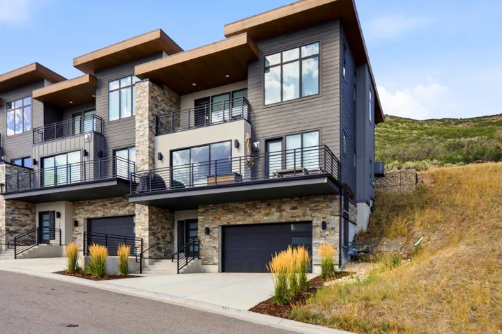 Modern townhome exterior featuring stone accents, dark siding, multiple balconies with metal railings, and attached garage