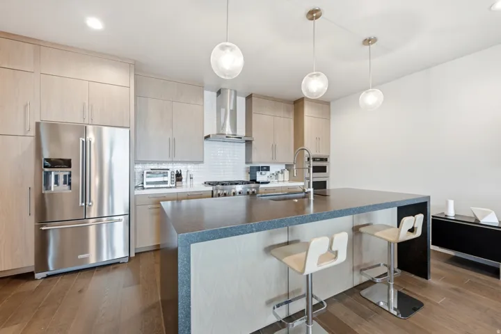 Gourmet kitchen featuring stainless steel appliances, a center island with seating, pendant lighting, custom cabinetry, and wood-finish flooring