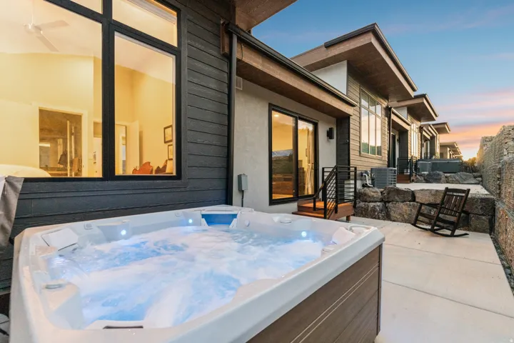 Outdoor hot tub with integrated lighting, concrete patio, modern exterior siding, rock retaining wall, and multiple exterior access points