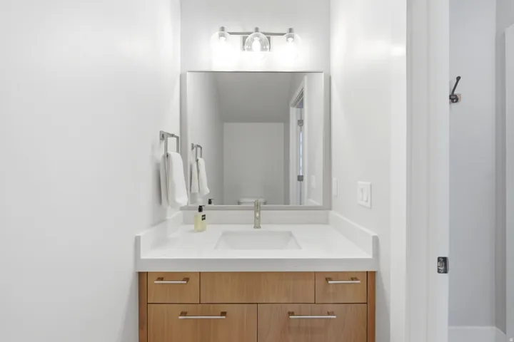 Light wood-finish vanity with drawer and cabinet storage, under-mount sink, and a white countertop