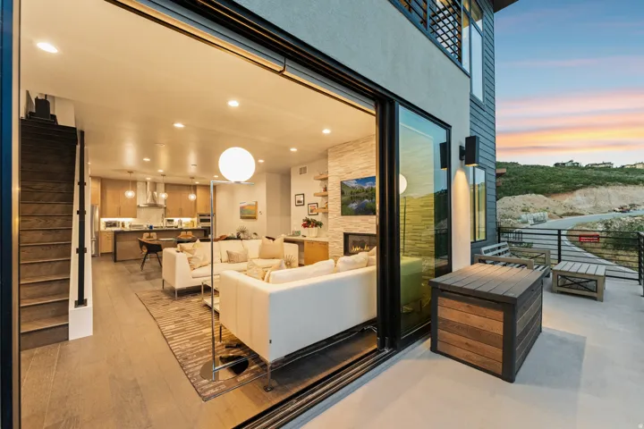 Sliding glass door leading to a concrete patio, wood-finish flooring, recessed lighting, and a kitchen featuring a stainless steel range hood