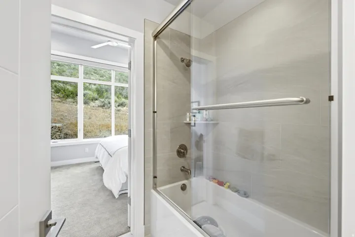 Tub and shower combination with a glass enclosure, tiled surround, and brushed metal fixtures