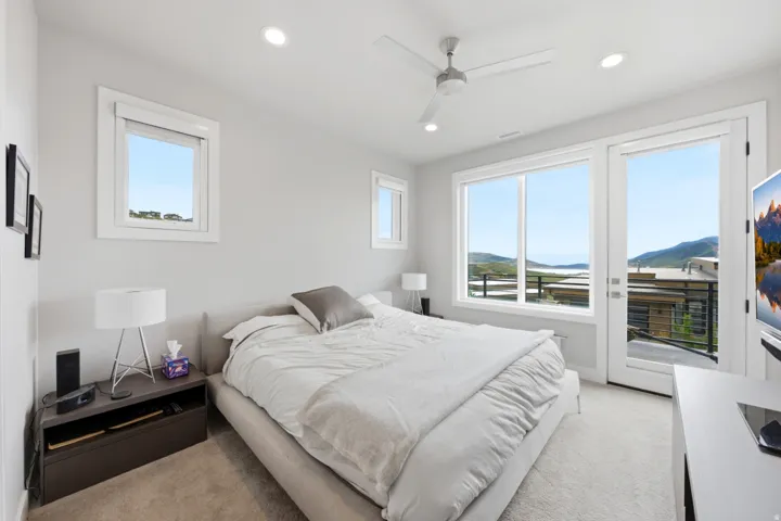 Recessed lighting and a ceiling fan illuminate a room with carpet flooring, a window, and a glass door opening to an exterior balcony
