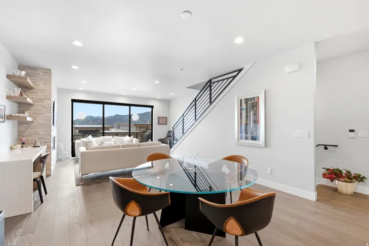 Open-concept living space with wood-finish flooring, a stacked stone fireplace, a built-in desk, and a staircase featuring a modern metal railing