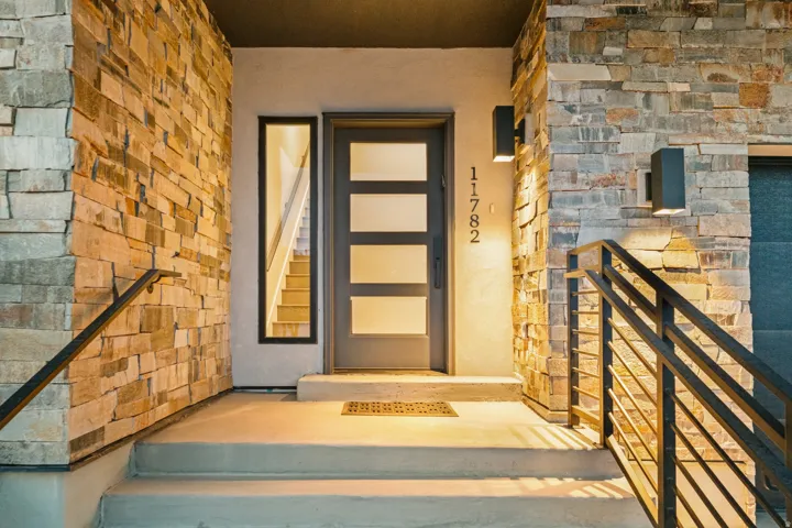 Stacked stone facade, modern entry door with frosted glass panels, concrete steps, and contemporary exterior lighting