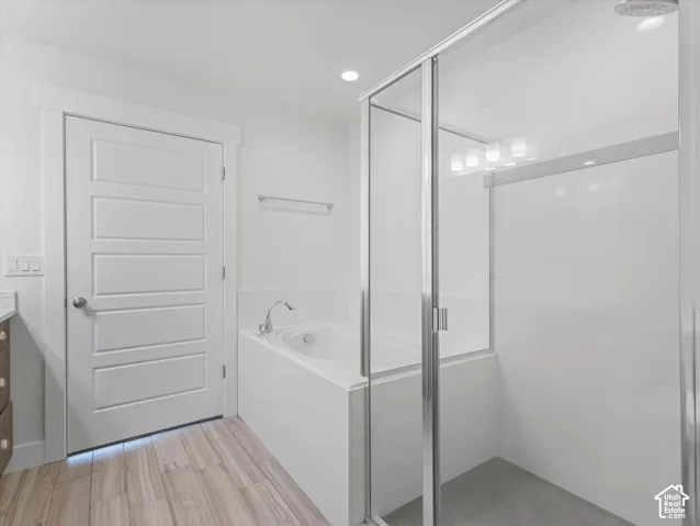 Spacious bathroom featuring a built-in soaking tub, glass-enclosed shower, wood-finish flooring, and a modern five-panel interior door