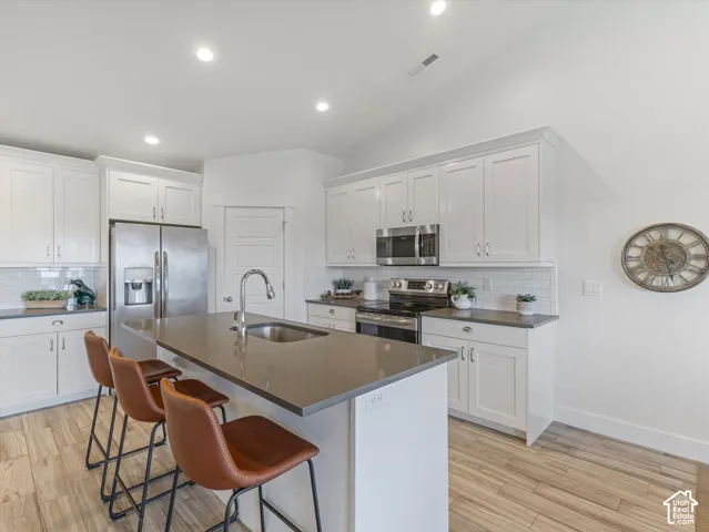 White shaker-style cabinetry, stainless steel appliances, wood-finish flooring, subway tile backsplash, and recessed lighting