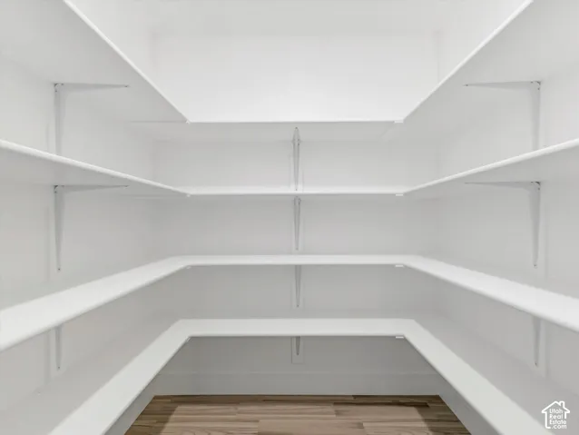 U-shaped pantry featuring multiple white shelves and wood-finish flooring