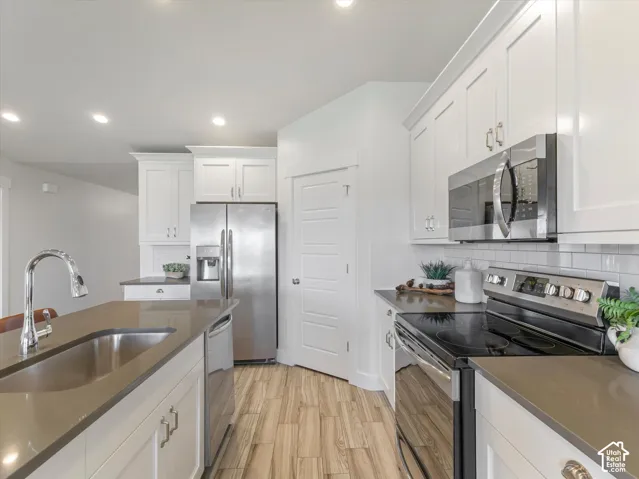 Kitchen featuring white cabinetry, stainless steel appliances, wood-finish flooring, subway tile backsplash, and recessed lighting