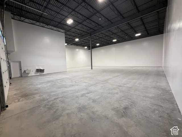 Warehouse, concrete flooring, tall white walls, and exposed ceiling trusses with integrated lighting
