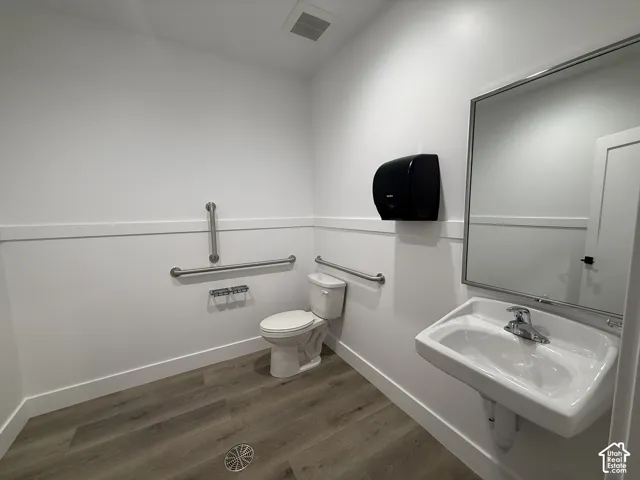 Warehouse Bathroom, Wall-mounted sink with chrome faucet, large framed mirror, wood-finish flooring, and white paneled walls