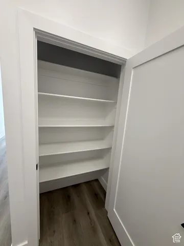 White interior door with a black handle, featuring a closet with white built-in shelving, and wood-finish flooring