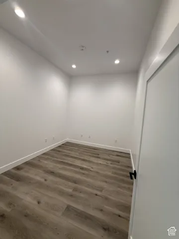 Recessed lighting, wood-finish flooring, white walls, and a white door with a black handle