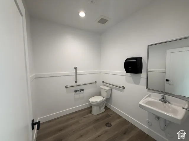 Wall-mounted sink, flush-mounted lighting, wood-finish flooring, white walls, and wainscoting