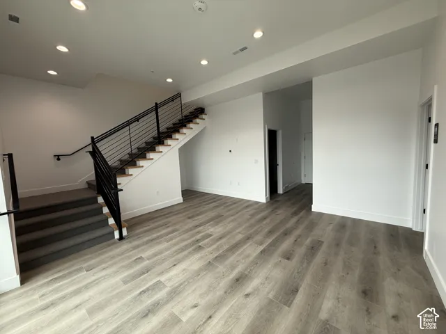 Hardwood-look flooring, recessed lighting, white walls, and a staircase with metal railings