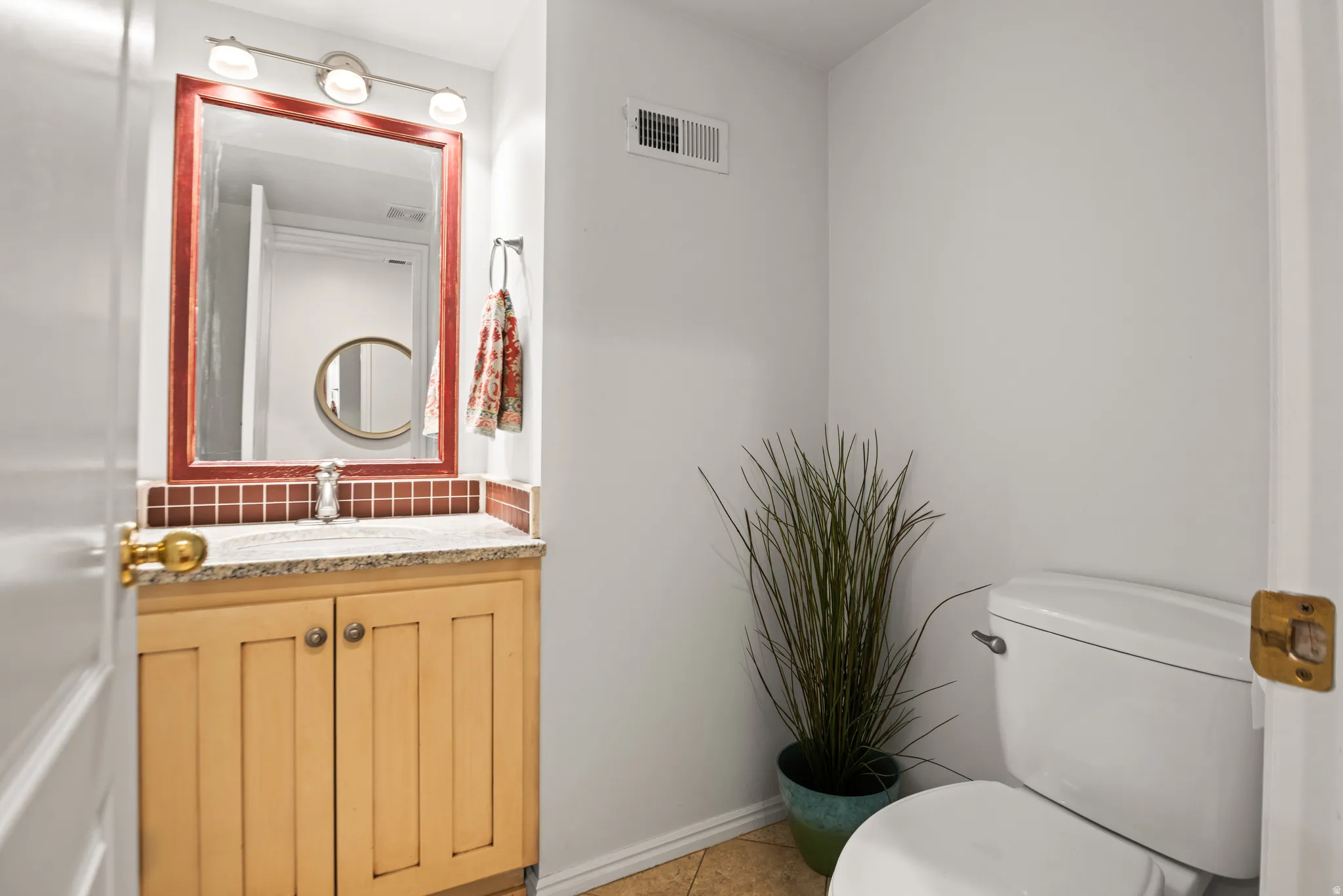 Cabinetry with gold-toned hardware, white toilet, vanity with granite-style countertop, wall-mounted mirror, and tile flooring