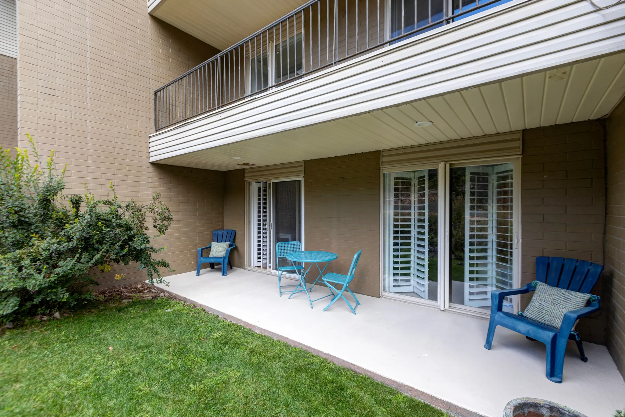 Ground-level patio with sliding glass doors, white louvered shutters, and a brick exterior
