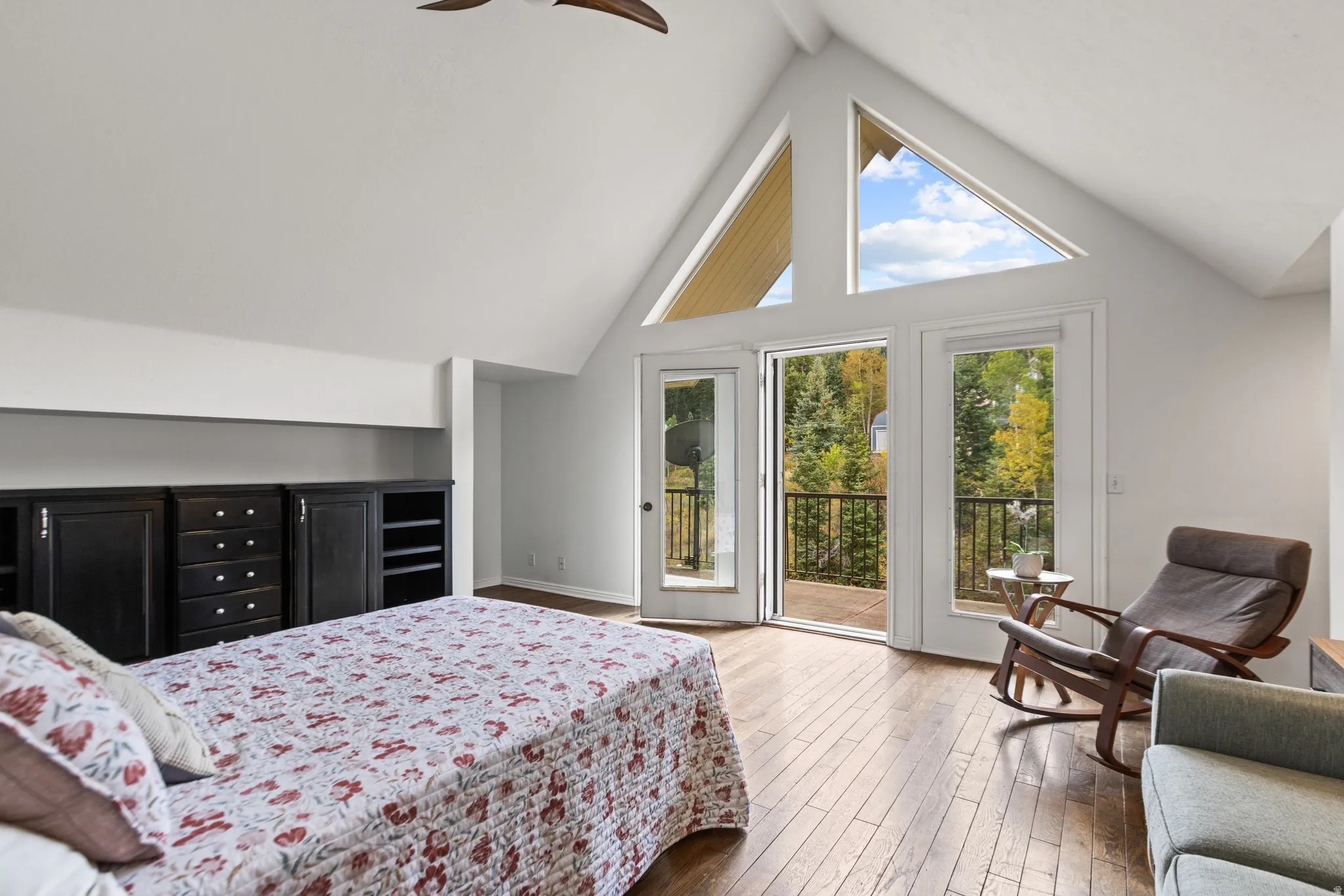 Vaulted ceilings with triangular windows, wood-finish flooring, built-in cabinetry, and a balcony with metal railings