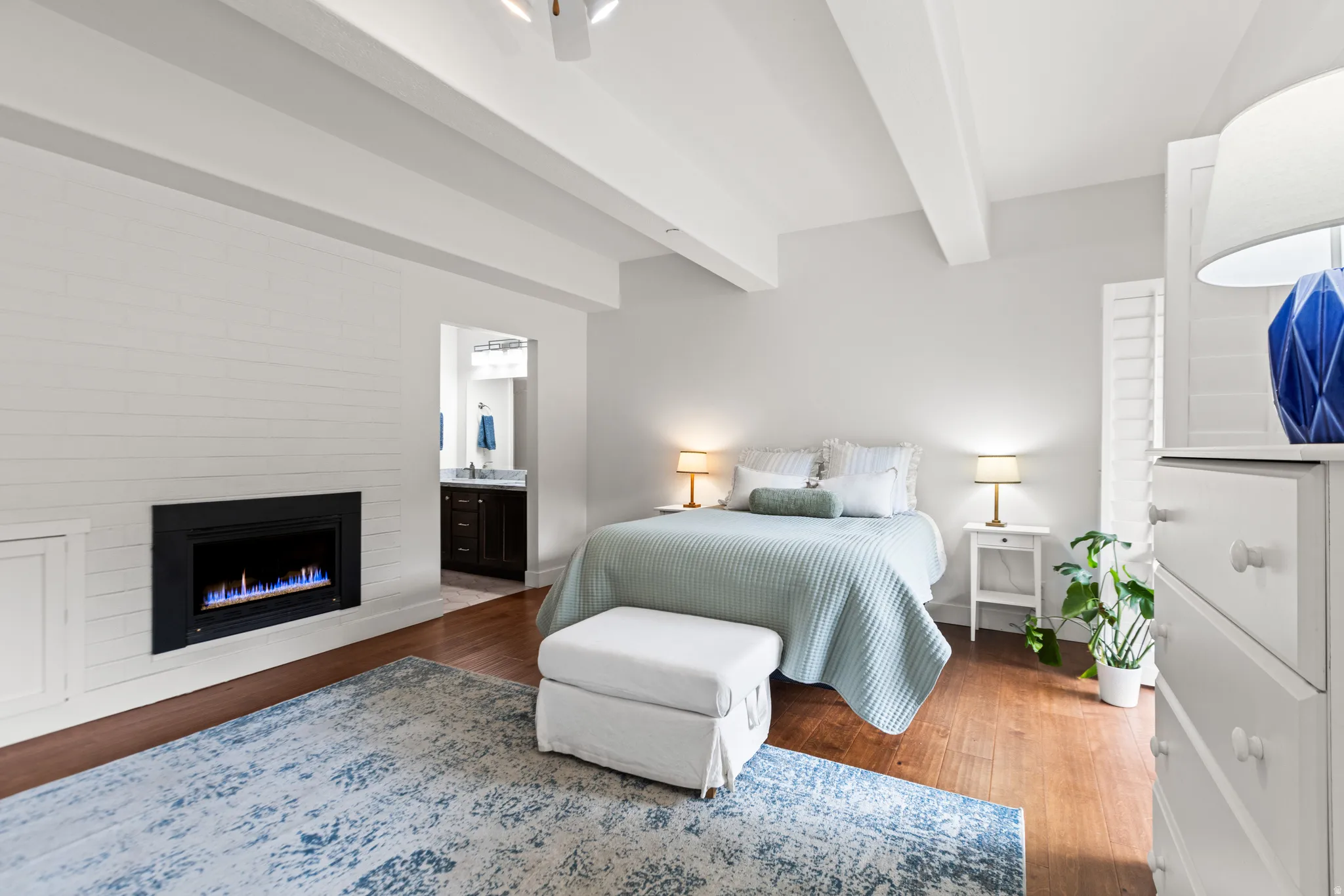 Hardwood flooring, exposed ceiling beams, recessed fireplace with an electric insert, and white plantation shutters