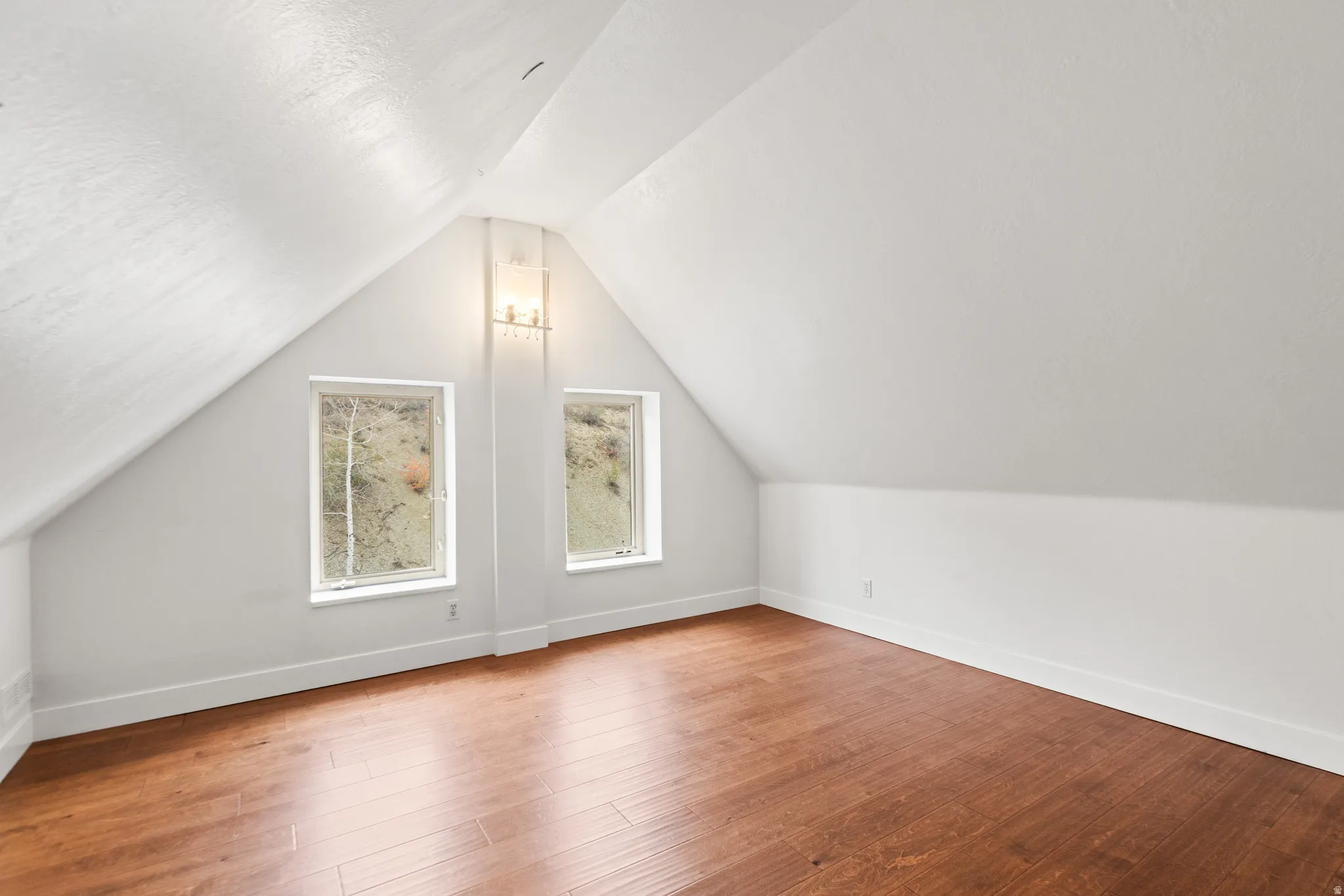 Wood-finish flooring, dual windows, and an overhead light fixture within an attic space