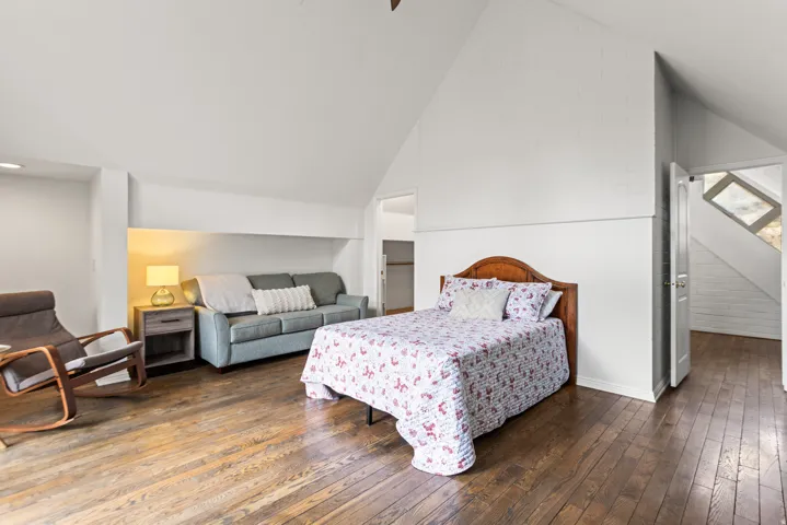 Vaulted ceiling, wood-finish flooring, built-in shelving, white painted brick accent wall, and a solid wood door