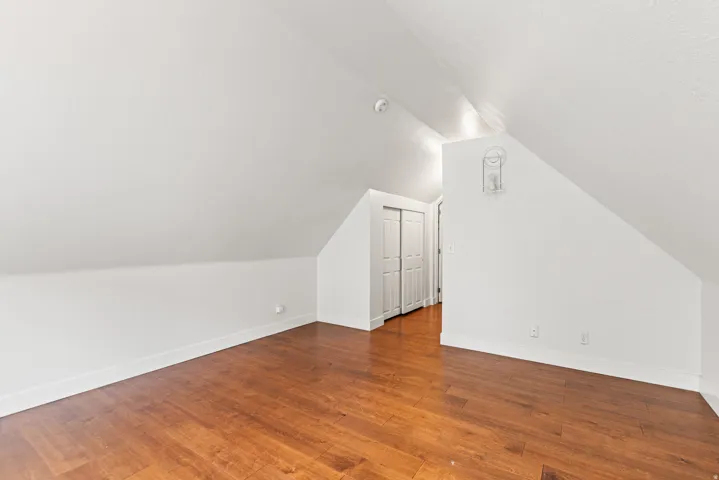 Sloped ceiling room featuring wood-finish flooring, white walls, and bi-fold closet doors