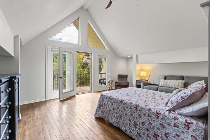 Vaulted ceiling with triangular windows, wood-finish flooring, and French doors opening to a balcony