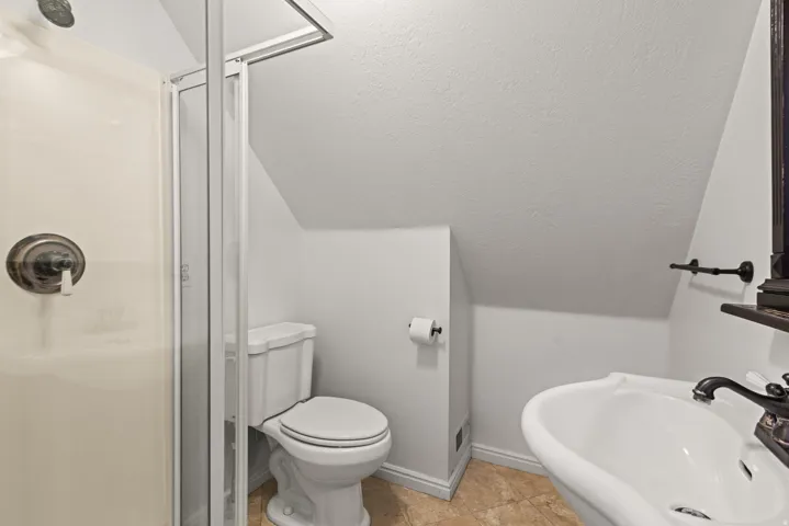 Shower enclosure with an oil-rubbed bronze fixture, pedestal sink, and textured flooring