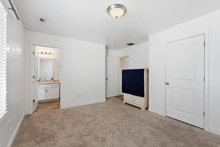 Carpeted flooring with white trim, a bathroom with wood-finish flooring, a single vanity with a light fixture, and a window with blinds