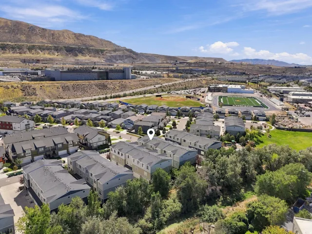 Aerial perspective of a residential community with multi-story townhomes, surrounding green spaces, and athletic fields