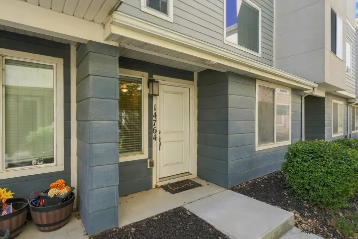 Exterior entry with a white door, concrete walkway, and dark mulch landscaping