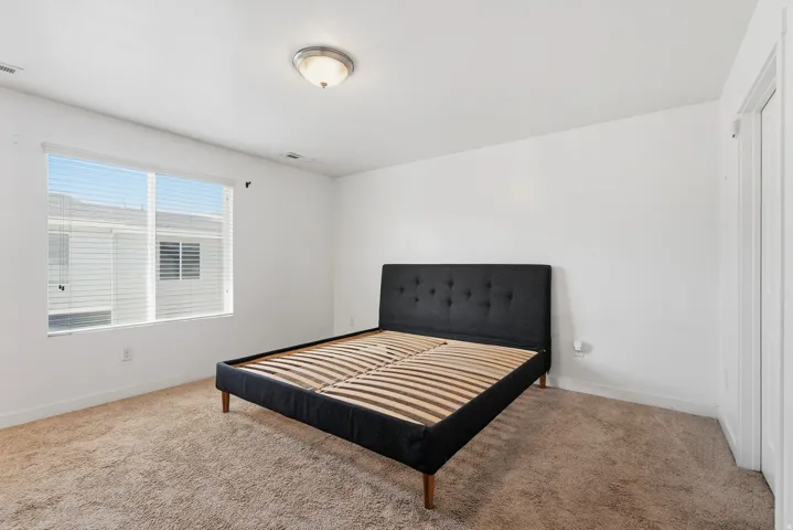 Neutral tone wall finishes, ceiling-mounted light fixture, carpeted flooring, and a window with horizontal blinds