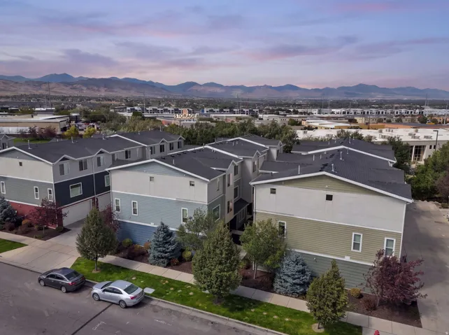 Multi-level townhome architecture with a dark shingle roof, a two-tone facade, and mature landscaping
