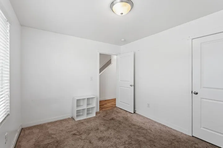 Wall-to-wall carpeting with white walls, a flush mount ceiling light, and a window with horizontal blinds