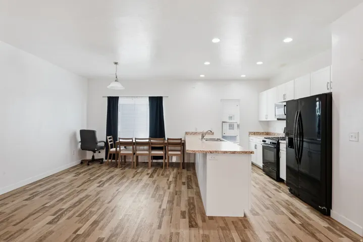 Open-concept living space with wood-finish flooring, recessed lighting, and a kitchen island featuring a stainless steel sink