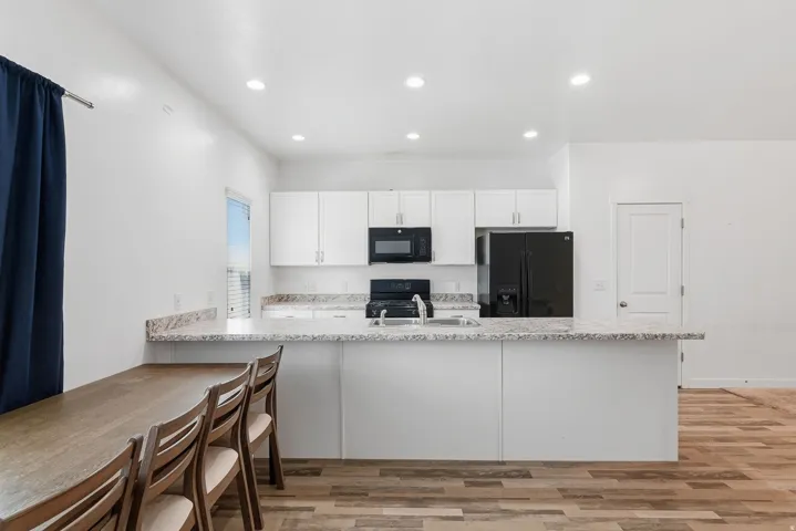 Kitchen with white cabinetry, speckled countertops, recessed lighting, and wood-finish flooring