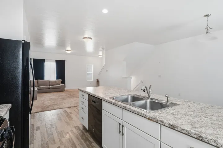 Kitchen island with a double basin stainless steel sink, a gray speckled countertop, and white cabinetry