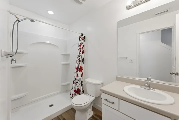 Bathroom featuring a shower stall with built-in shelving, a single vanity with an integrated sink, and wood-finish flooring
