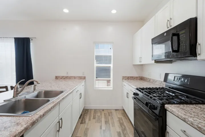 Kitchen with white cabinetry, wood-finish flooring, a double basin stainless steel sink, and a black built-in microwave and range