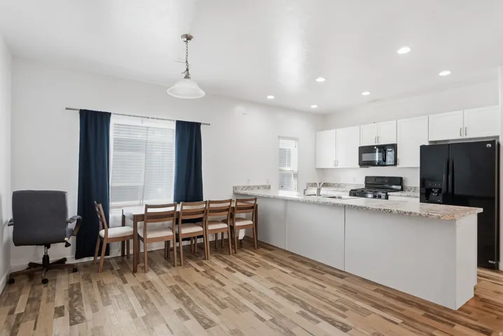 Kitchen featuring white cabinetry, granite countertops, black appliances, and wood-finish flooring