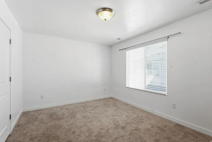 Neutral wall color, window with blinds, carpeted flooring, and a flush-mount ceiling light fixture