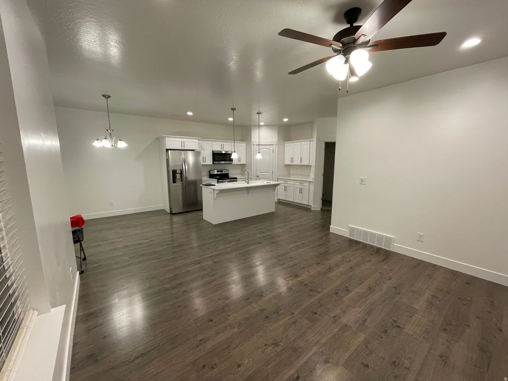 Open-concept living area featuring wood-finish flooring, a contemporary ceiling fan, and a kitchen with white cabinetry, stainless steel appliances, and an island