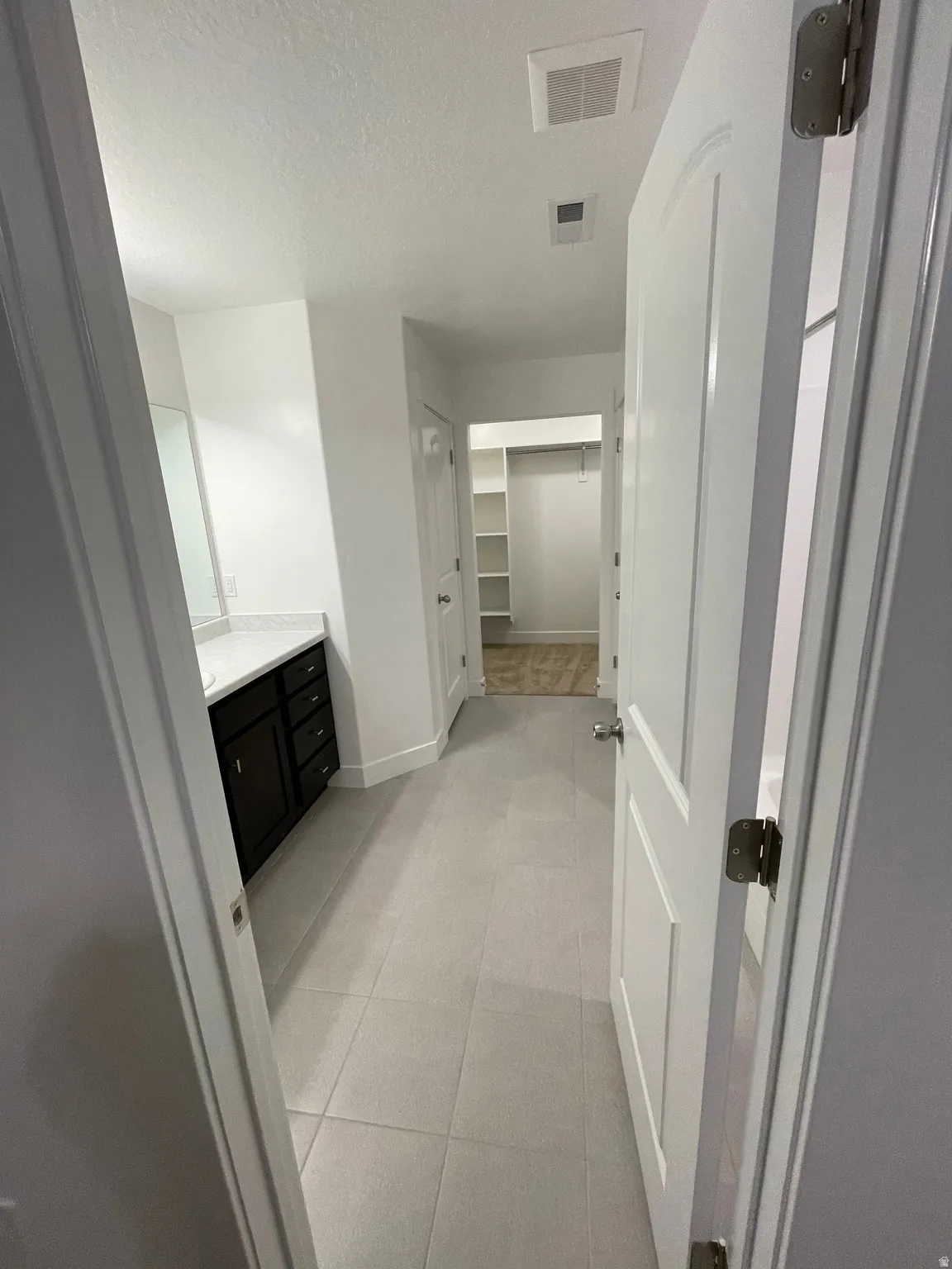 Hallway featuring light-toned tile flooring, a dark wood-finish vanity with a light-toned countertop, and a walk-in closet with built-in shelving