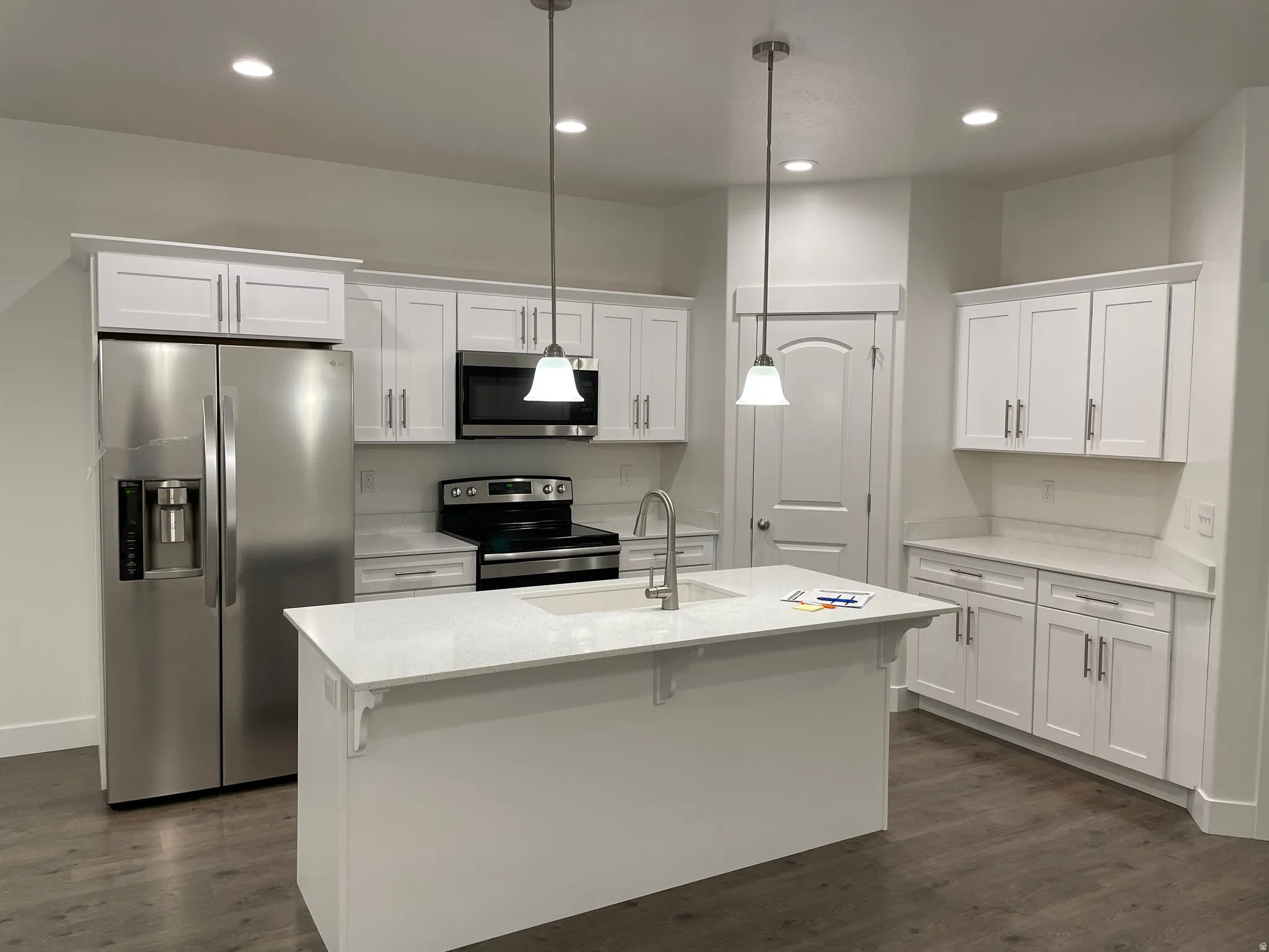 Kitchen featuring a large island with an integrated sink, white cabinetry, stainless steel appliances, light-colored countertops, and wood-finish flooring
