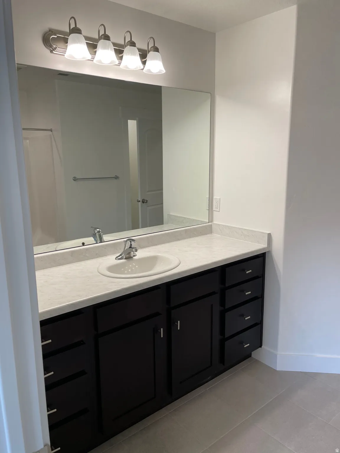 Spacious vanity with a light-toned countertop, undermount sink, dark-finish cabinetry, and a prominent wall mirror