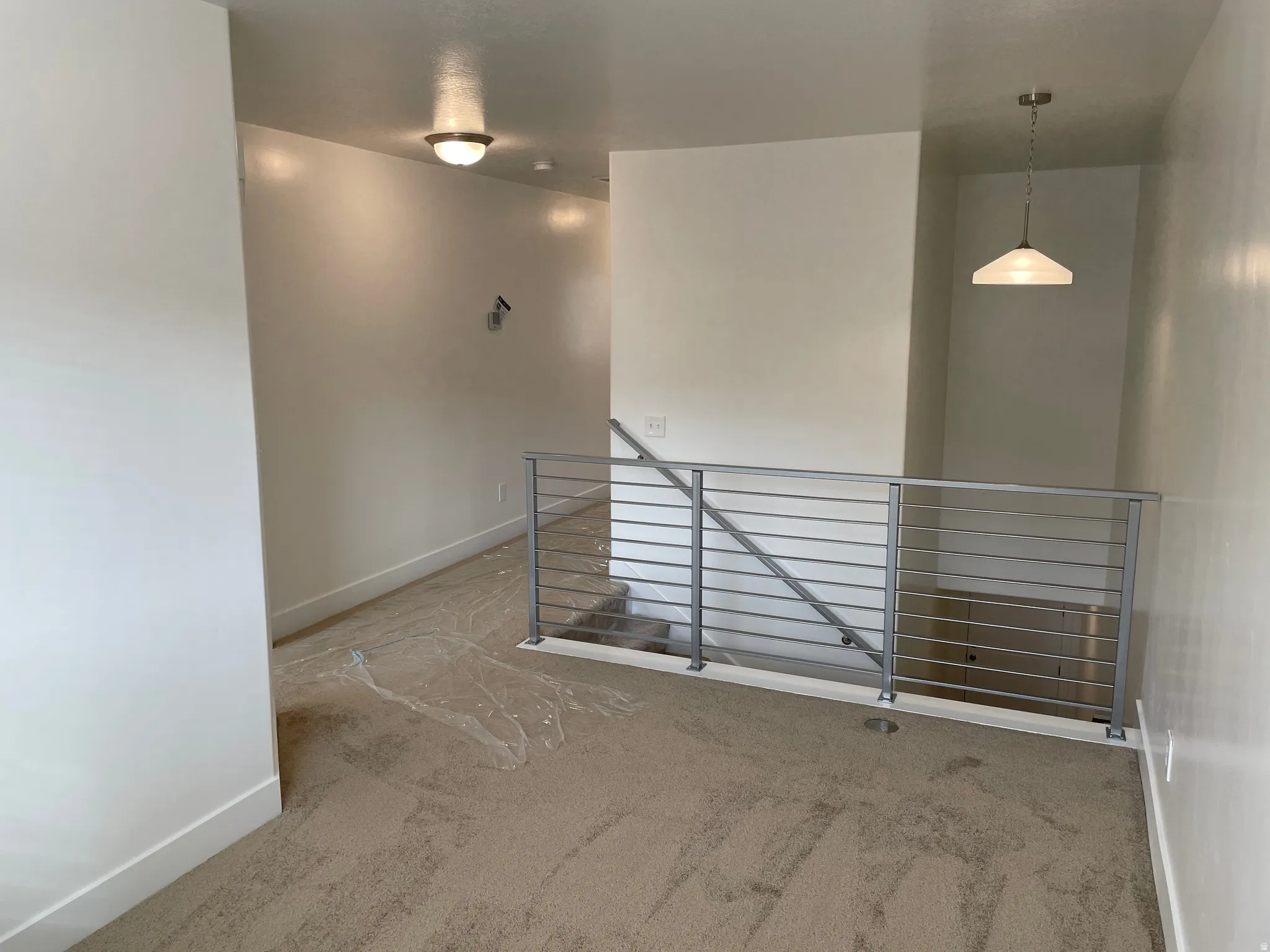 Carpeted landing with modern horizontal metal railing, overhead flush mount lighting, and a pendant light fixture